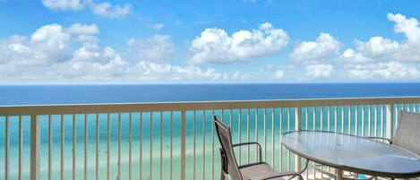 A balcony with a view of the ocean, a table, and a chair.