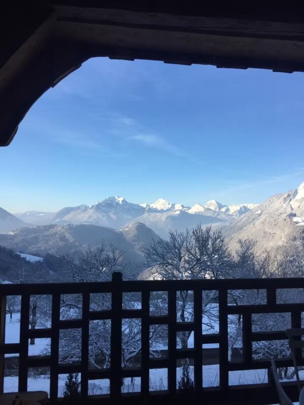 Vista desde una ventana con baranda de madera, con montañas nevadas y cielo despejado.