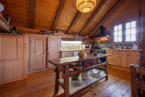 A rustic kitchen with wooden cabinets, a wooden table, and a hanging light fixture. - Exceptional Chalet - Panoramic View - Sauna - Aravis (Serraval)