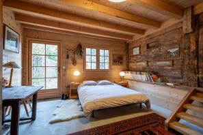Acogedor dormitorio de cabaña de madera con una cama, dos lámparas de noche, un escritorio de madera y una ventana con vistas a árboles.
