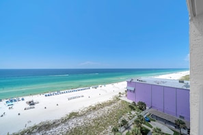 Blick auf einen Strand mit blauem Himmel, sandigem Ufer und einem violetten Gebäude.
