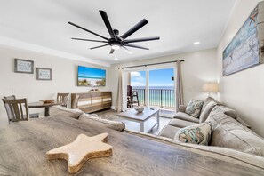 A spacious living room with a large wooden table, a ceiling fan, and a view of the ocean through a sliding glass door. - The Summit 1109 (Panama City Beach)