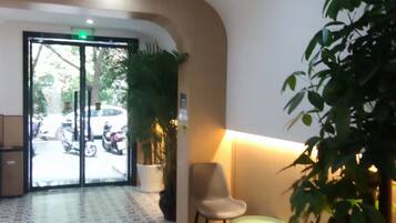 A lobby with patterned flooring, a seating area with chairs, a potted plant, and a glass door leading outside.
