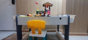 Zona de juegos para niños con una mesa pequeña, una silla amarilla y una estructura de juguete con forma de casa.