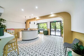 Un área de recepción con un mostrador curvo, una zona de estar con sillones, una planta en maceta y vistas al exterior a través de puertas de vidrio grandes.