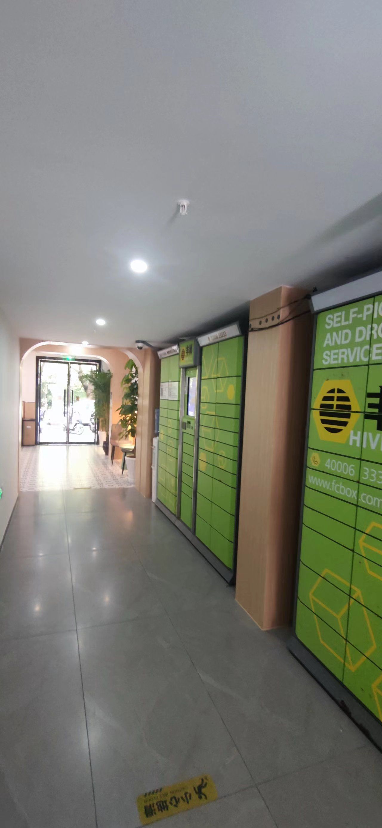 A hallway with green lockers, a sign for self-service and drop-off, and a door leading outside.