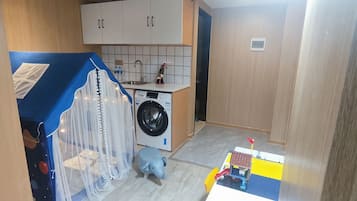 Een functionele keuken met een wasmachine, een spoelbak en een hoekje voor kinderen met een speelgoedauto en een blauw speeltje.