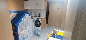 Uma cozinha compacta com máquina de lavar, pia e um pequeno espaço de recreação com um carrinho de brinquedo e um brinquedo azul.