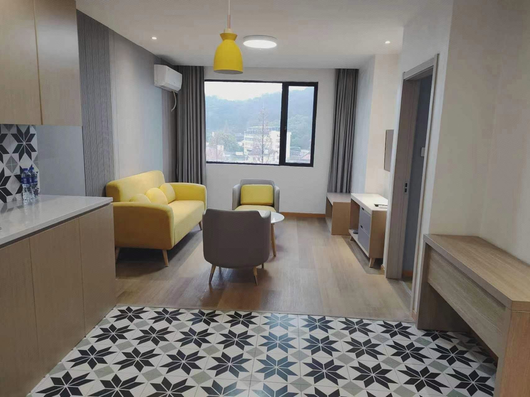 A modern living room with a sofa, a chair, a small table, and a view of a cityscape through a large window.
