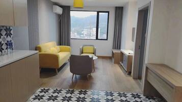 A modern living room with a sofa, a chair, a small table, and a view of a cityscape through a large window.