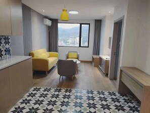 Un saló modern amb un sofà, una cadira, una taula petita i una vista d'un paisatge urbà a través d'una finestra gran.