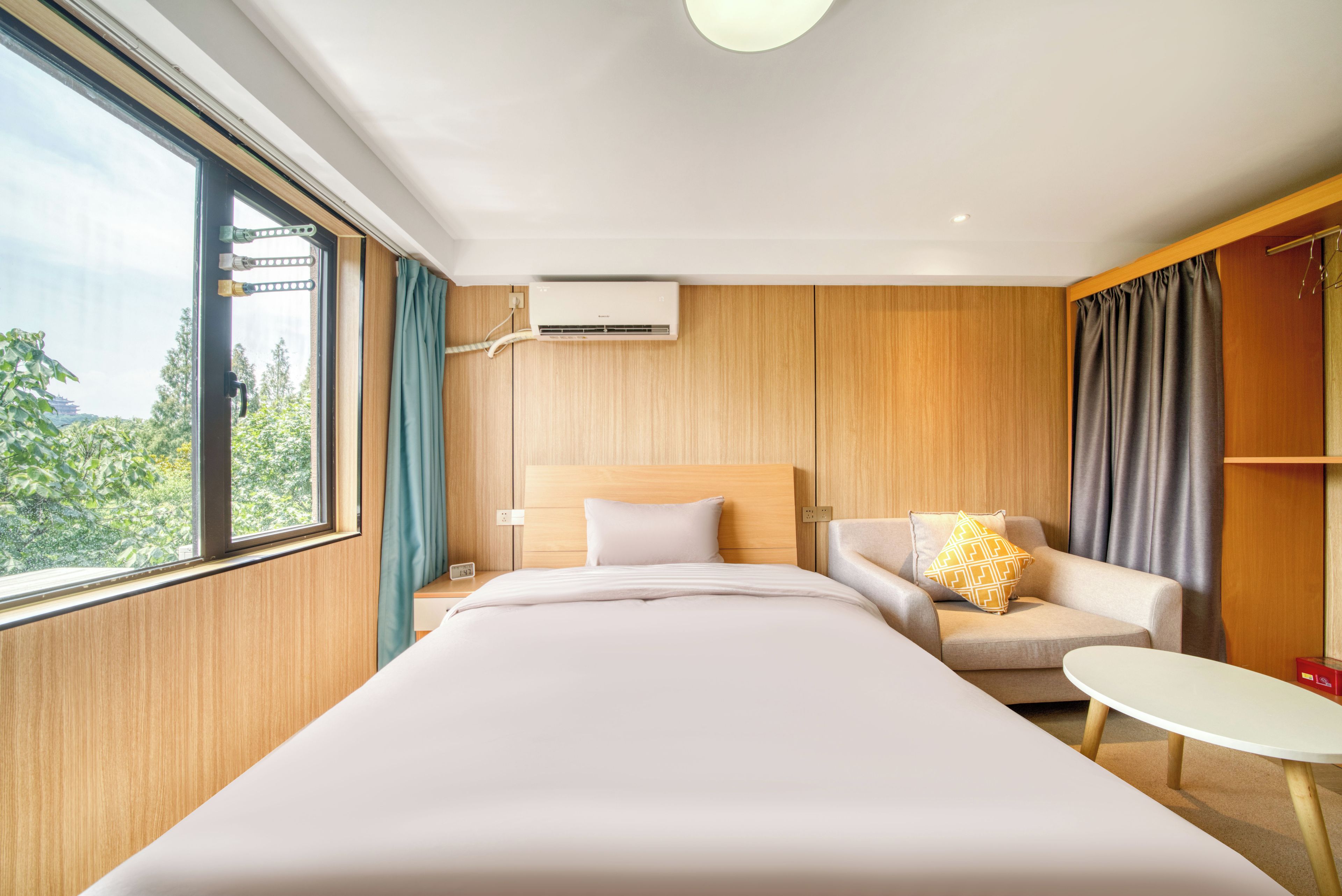 A hotel room with a bed, a sofa, a small table, and a view of greenery outside.