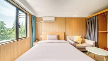 A hotel room with a bed, a sofa, a small table, and a view of greenery outside.