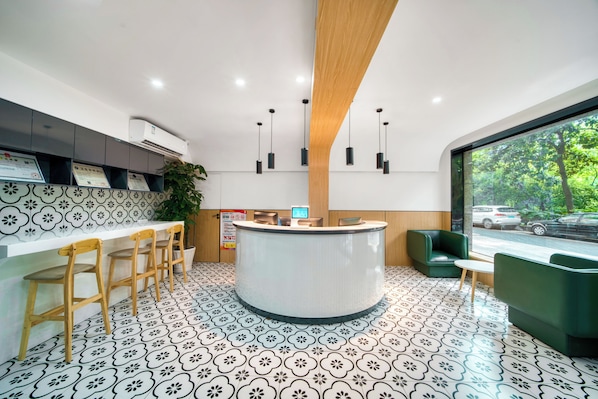 Uma área de recepção moderna com um balcão central, banquetas, um vaso de planta e vista para a rua através de uma grande janela.