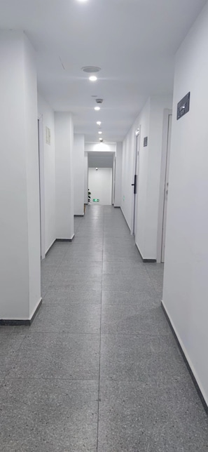 Um corredor com paredes brancas, chão em piso cinza e portas em ambos os lados.