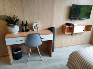 Quarto de hotel com escrivaninha de madeira, uma cadeira, televisão, cama e uma pequena estante com telefone.