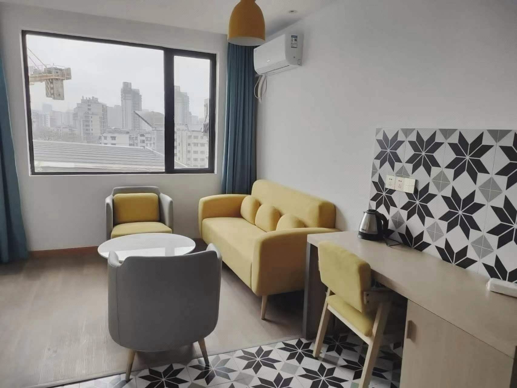 A modern hotel room with a sofa, two chairs, a small table, and a decorative wall panel.