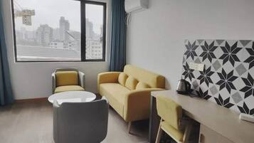 A modern hotel room with a sofa, two chairs, a small table, and a decorative wall panel.