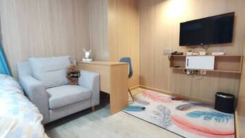 A hotel room with a sofa, a desk, a television, and a small decorative item.
