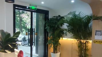 A reception area with a white reception desk, potted plants, and a patterned floor.