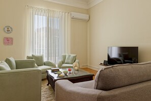 A living room with a sofa, two armchairs, a coffee table with decorative items, a flat-screen TV, and a large window with sheer curtains. - Vesta - Luxury APT - 2BR - Zamalek II (Cairo)