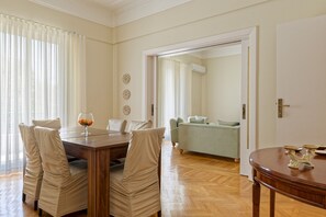 A dining area with a wooden table and chairs, a glass bowl of fruit, and a sofa in the background. - Vesta - Luxury APT - 2BR - Zamalek II (Cairo)