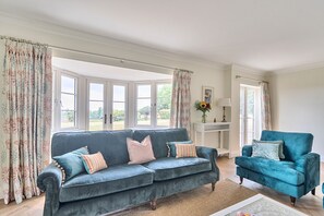 A living room with a blue sofa, a matching armchair, and a small table with a vase of flowers. - Summerfield House, Blandford Forum, Wimborne (Blandford Forum)