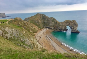 A coastal landscape with a prominent rock formation arching over the beach, a sandy shoreline, and a grassy hill. - Summerfield House, Blandford Forum, Wimborne (Blandford Forum)