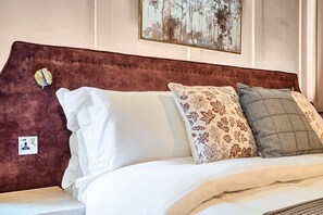 Ein Bett mit braun gepolstertem Kopfteil, weißer Bettwäsche und zwei gemusterten Kissen.