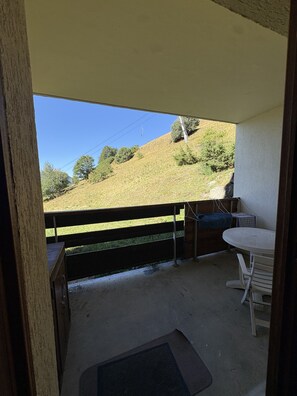 A balcony with a view of a grassy hillside, a wooden railing, and a small table with chairs. - Cabin studio with mountain view (Orcières)