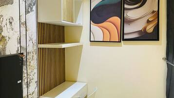 A modern hotel room with a white desk, a chair, a bed, and two abstract paintings on the wall.