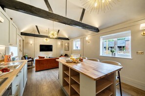 A modern kitchen with a wooden island, built-in appliances, and a dining area with a sofa. - Willow Brook, Hamptworth, Hampshire (Salisbury)