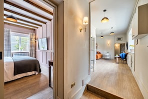 Une chambre d’hôtel avec un lit, une fenêtre avec des rideaux, un téléviseur fixé au mur et un escalier menant à une autre pièce.