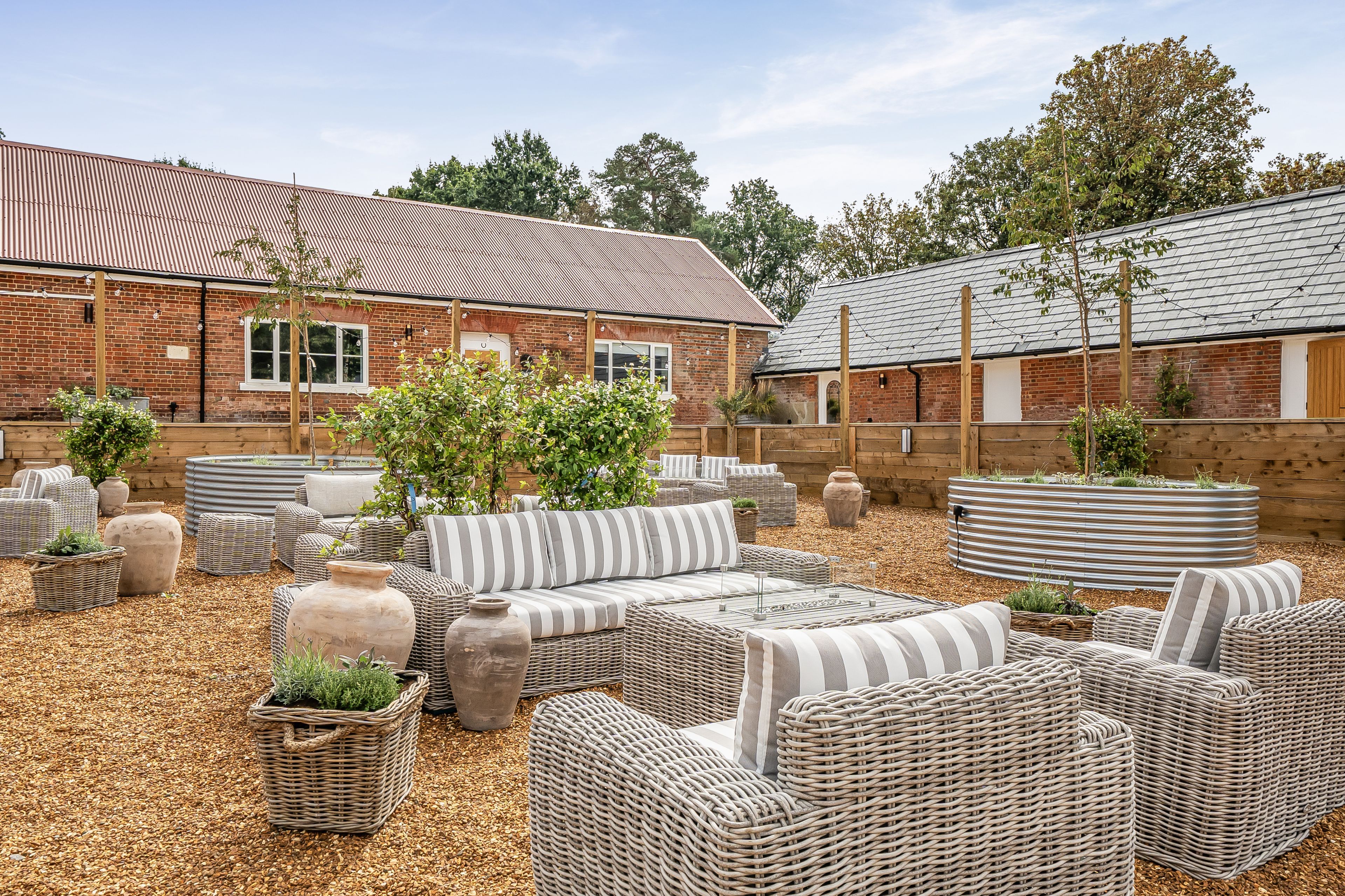 Une cour avec du mobilier d’extérieur, un bâtiment en briques et des arbres.