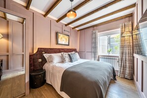A bedroom with a wooden ceiling, a bed with a headboard, a bedside table, and a window with curtains. - Foxglove Cottage, Hamptworth, Hampshire (Salisbury)