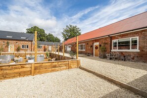 Une cour avec un sol de gravier, des bancs en bois et un bâtiment en briques surmonté d’un toit rouge.