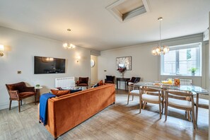 A modern living room with a large sofa, a dining area with a glass table, and a kitchen in the background. - Fern Cottage, Hamptworth, Hampshire (Salisbury)
