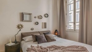 A bedroom with a bed, bedside tables, a mirror, wall decorations, and a window with curtains. - MODERN 3-BEDROOM FLORENCE HOME NEAR DUOMO & PIAZZA DELLA REPUBBLICA (Firenze)