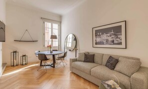 Un salon moderne avec un canapé, une table à manger et des chaises, une lampe et un tableau encadré accroché au mur.
