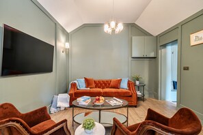 Ein Wohnzimmer mit einer Eckcouch, einem Flachbildfernseher, einer Chandelierleuchtre und einem Couchtisch mit Büchern und Früchten.