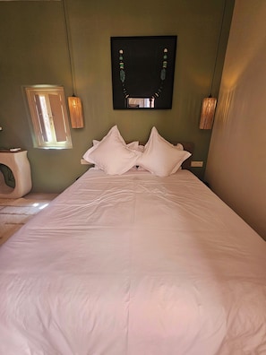 A neatly made bed with white linens and pillows, a bedside table with a lamp, and a wall-mounted mirror. - Riad Victoria (Marrakech)
