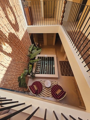 A multi-level atrium with a central staircase, a seating area with patterned cushions, and a decorative wall with a brick pattern. - Riad Victoria (Marrakech)
