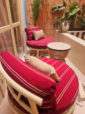 A seating area with a cushioned chair and a round table, a wicker basket, and a red and white striped sofa against a bamboo wall. - Riad Victoria (Marrakech)