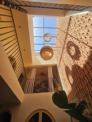 A multi-level interior with a skylight, a hanging circular light fixture, and a brick wall. - Riad Victoria (Marrakech)