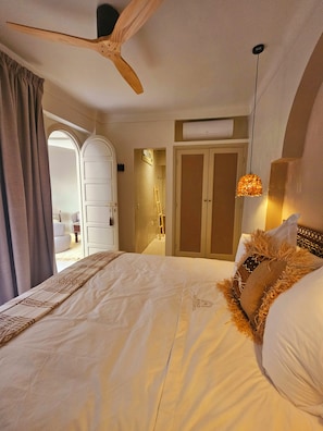 Habitació d'hotel amb un llit, un ventilador de sostre, un armari i una lluminària penjant.