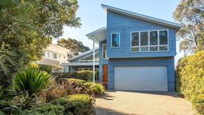 Une maison moderne à deux étages avec un garage, entourée d’une végétation luxuriante et dotée d’une allée pavée.
