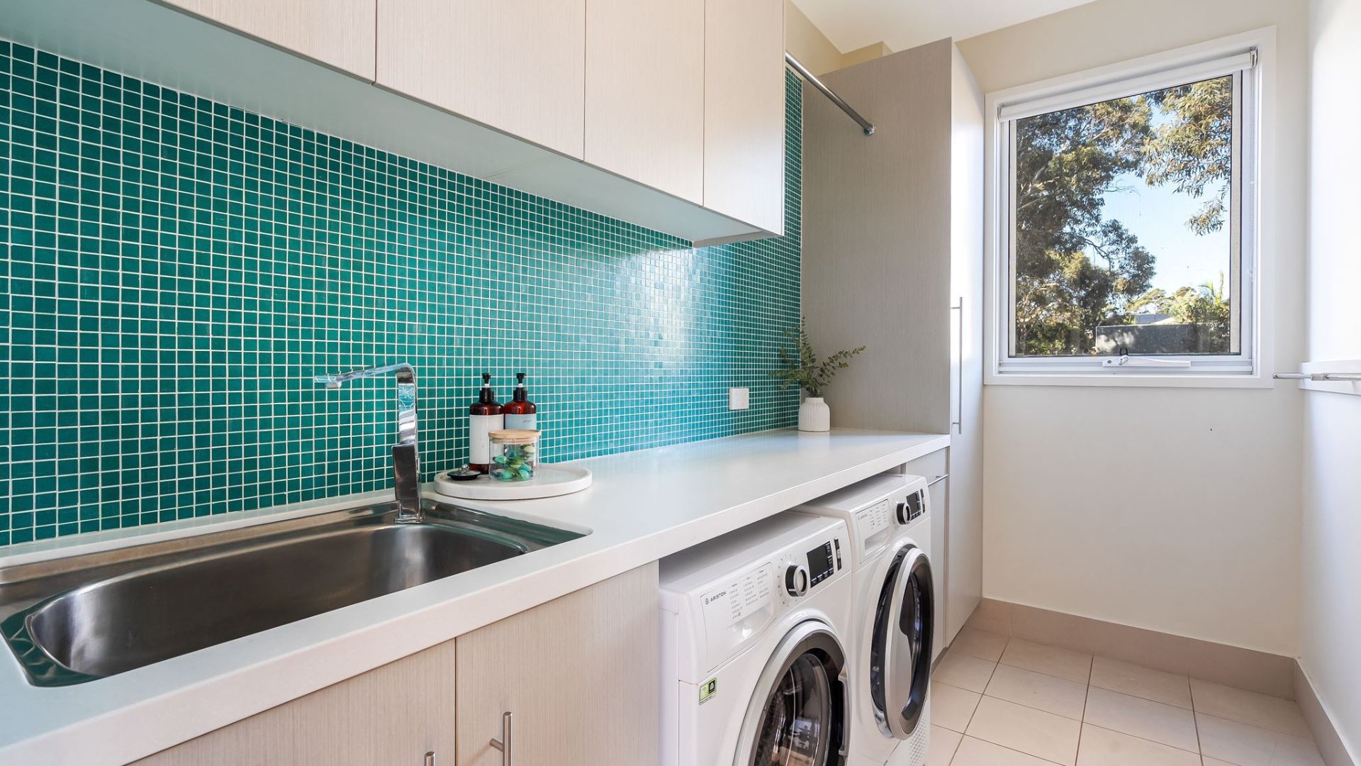 Una cocina con un lavabo, lavadora y ventana con vistas a árboles.