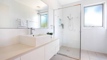 Un baño moderno con ducha envuelta en vidrio, un lavabo blanco y un espejo grande.