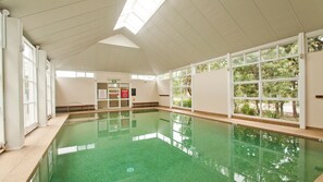 An indoor swimming pool with clear glass walls, a tiled floor, and a skylight ceiling. - Sapphire Sands – home base for a fun beach getaway (Callala Beach)