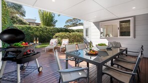 An outdoor patio with a grill, dining table, chairs, and a view of the garden. - Sapphire Sands – home base for a fun beach getaway (Callala Beach)